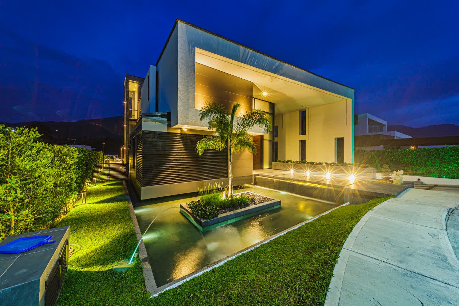 Casa moderna iluminada en hora azul, con espejo de agua y jardín