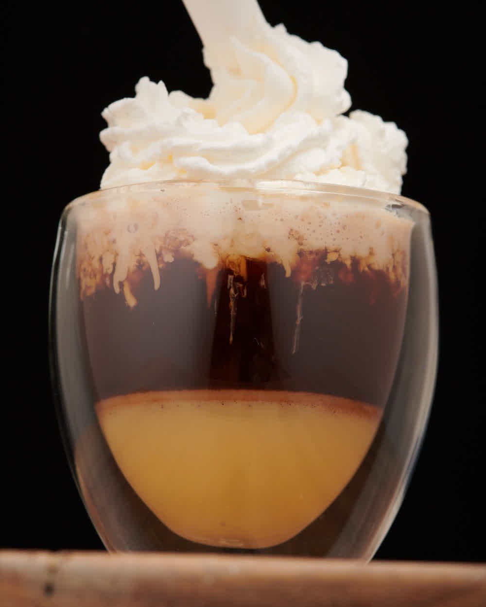 Vaso de café en capas con la crema montándose, sobre fondo negro